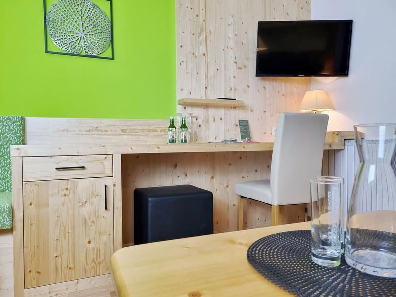 Ein Hotelzimmer mit Holzmöbeln, einem Schreibtisch, einem Fernseher an der Wand und einer grünen Wanddekoration.