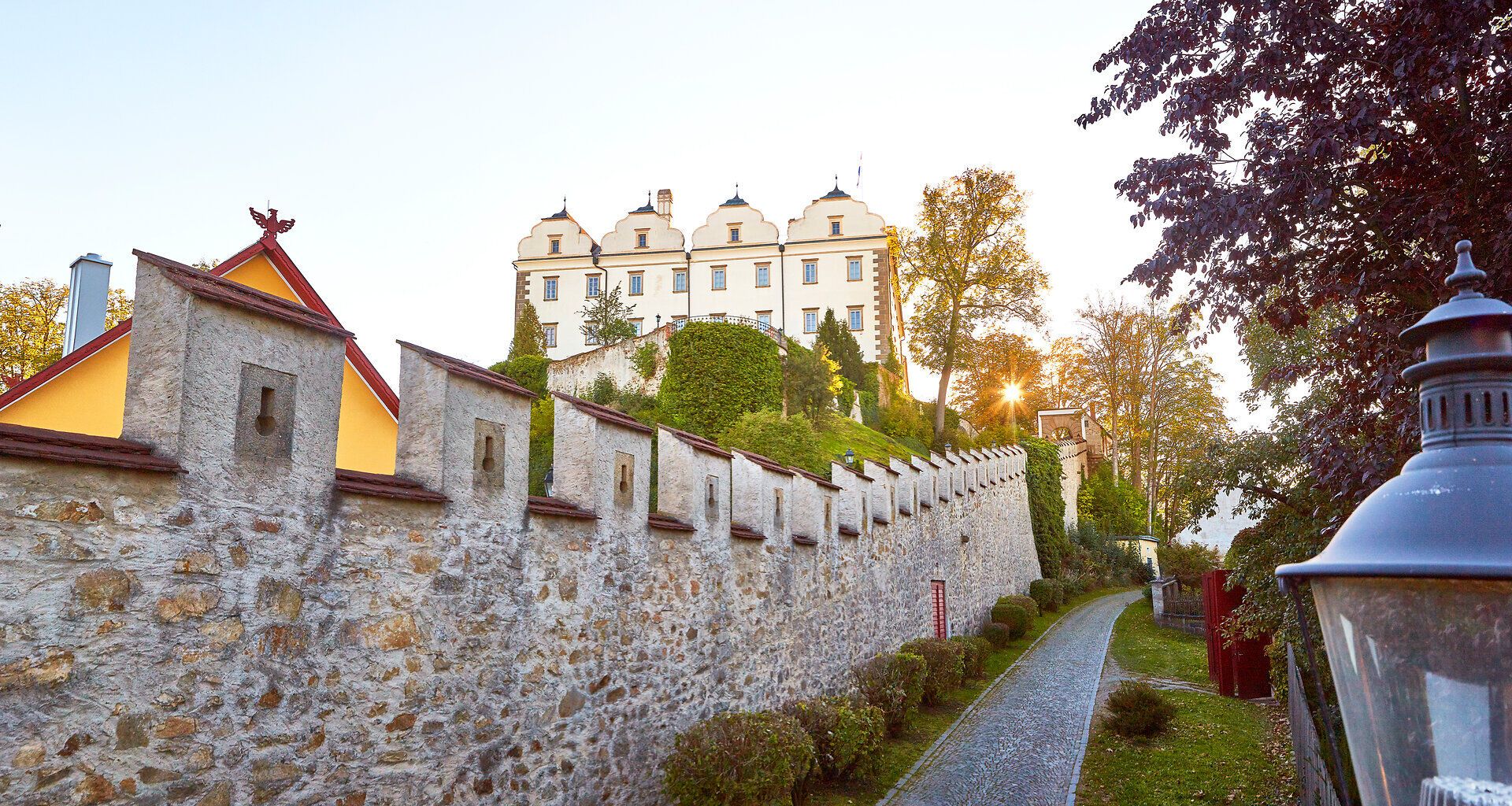 Das majestätische Schloss Weitra thront erhaben über der sanften Hügellandschaft und wird von der warmen Abendsonne in goldenes Licht getaucht. Die umgebenden Gärten und der alte Steinwall verleihen dem Ort eine romantische Atmosphäre, die zum Verweilen einlädt.