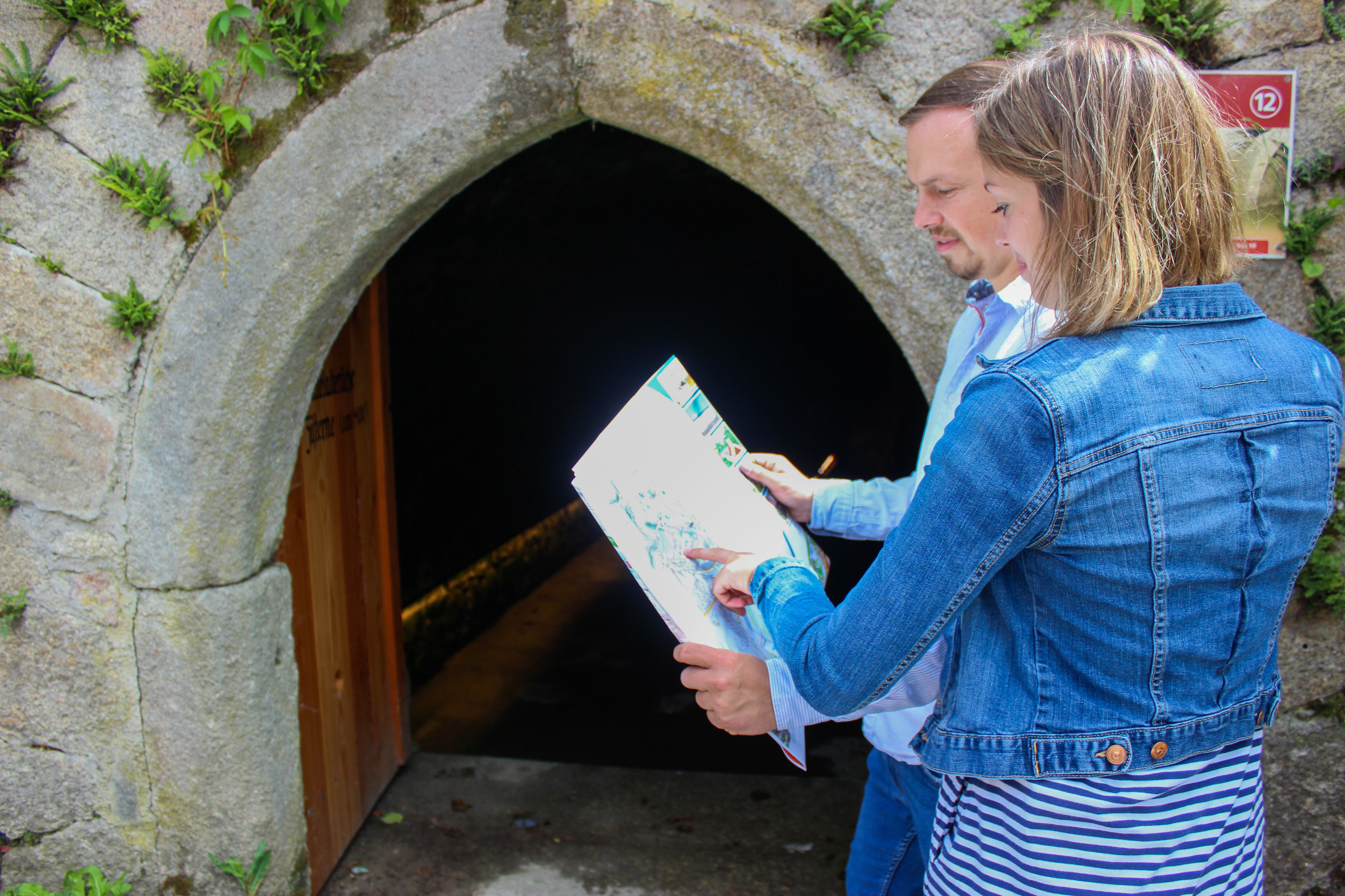 Ein Mann und eine Frau schauen sich einen Stadtplan an. Im Hintergrund der Eingang zur mittelalterlichen Zisterne in Weitra.