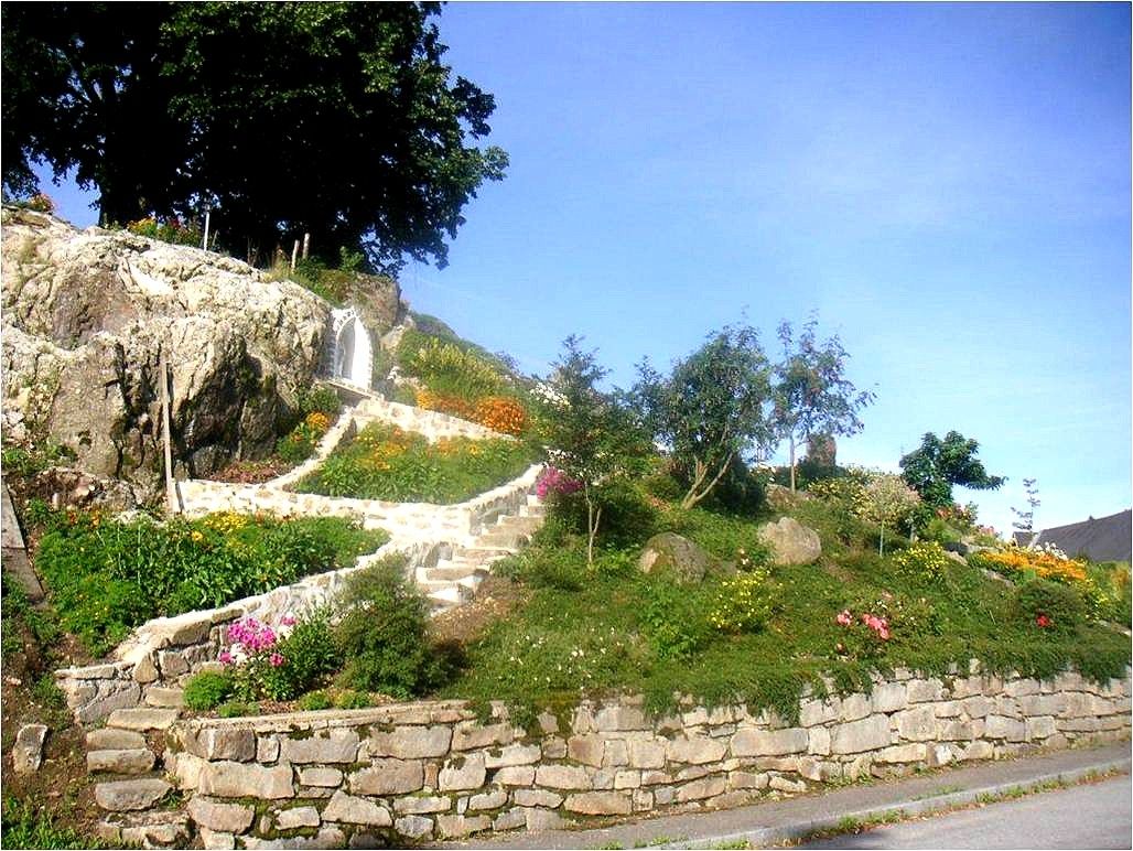 Steingarten mit Blumen und Treppe, umgeben von Bäumen.