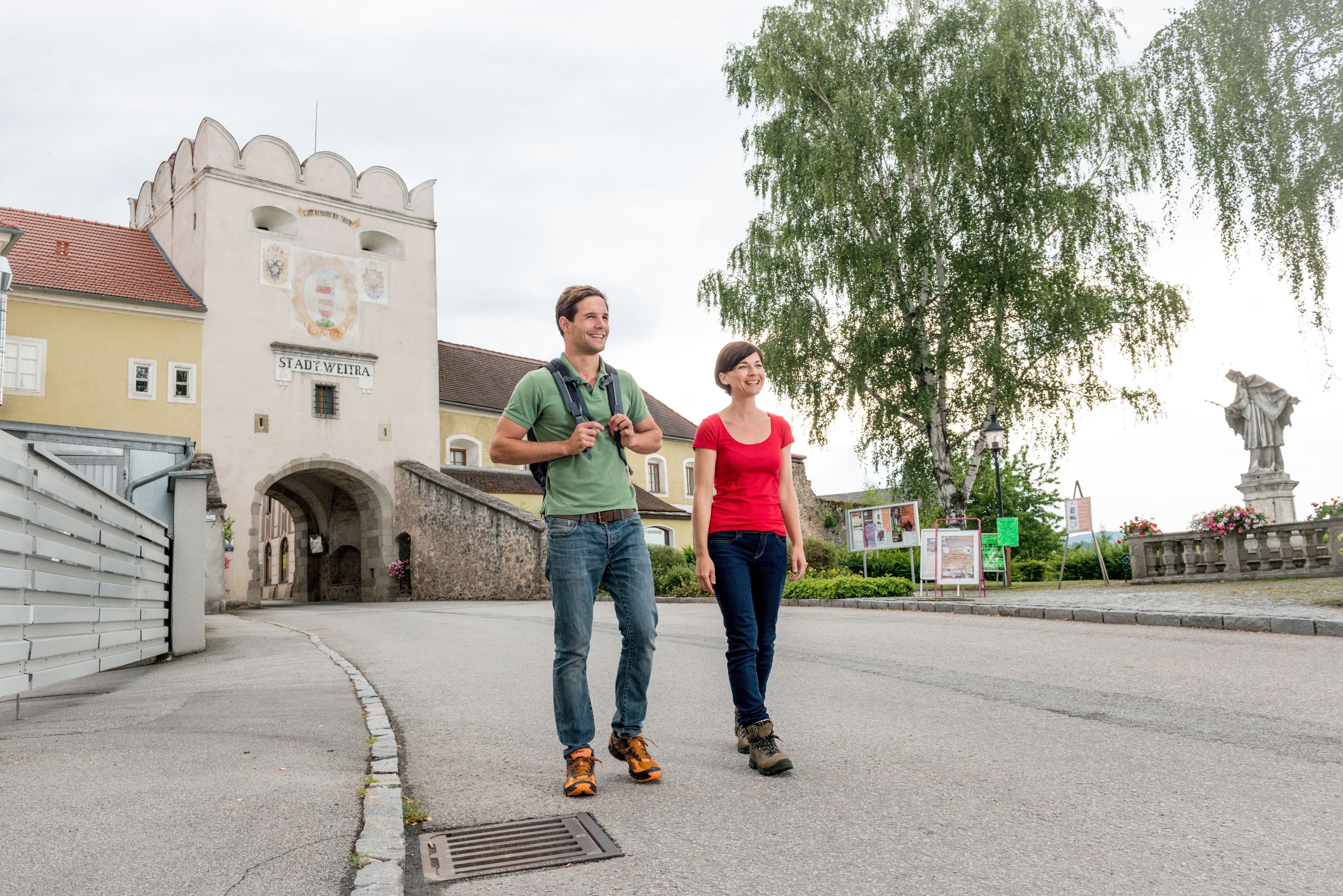 Ein Mann und eine Frau wandern, im Hintergrund das Stadttor von Weitra