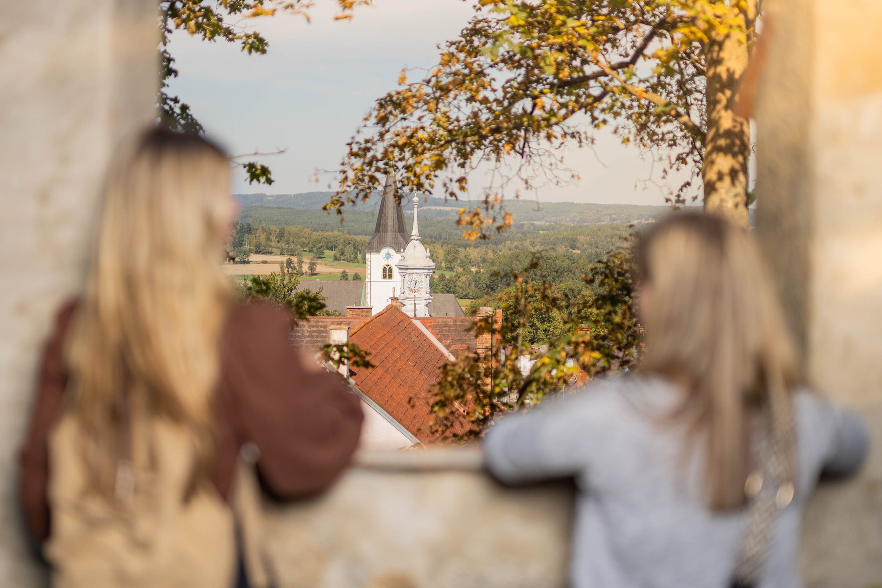 Zwei Frauen schauen zwischen zwei Zinnen auf die Altstadt von Weitra, im Hintergrund der Kirchturm der Pfarrkirche Weitra