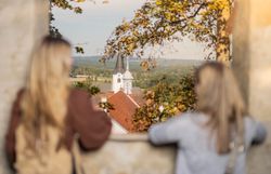 Zwei Frauen schauen zwischen zwei Zinnen auf die Altstadt von Weitra, im Hintergrund der Kirchturm der Pfarrkirche Weitra
