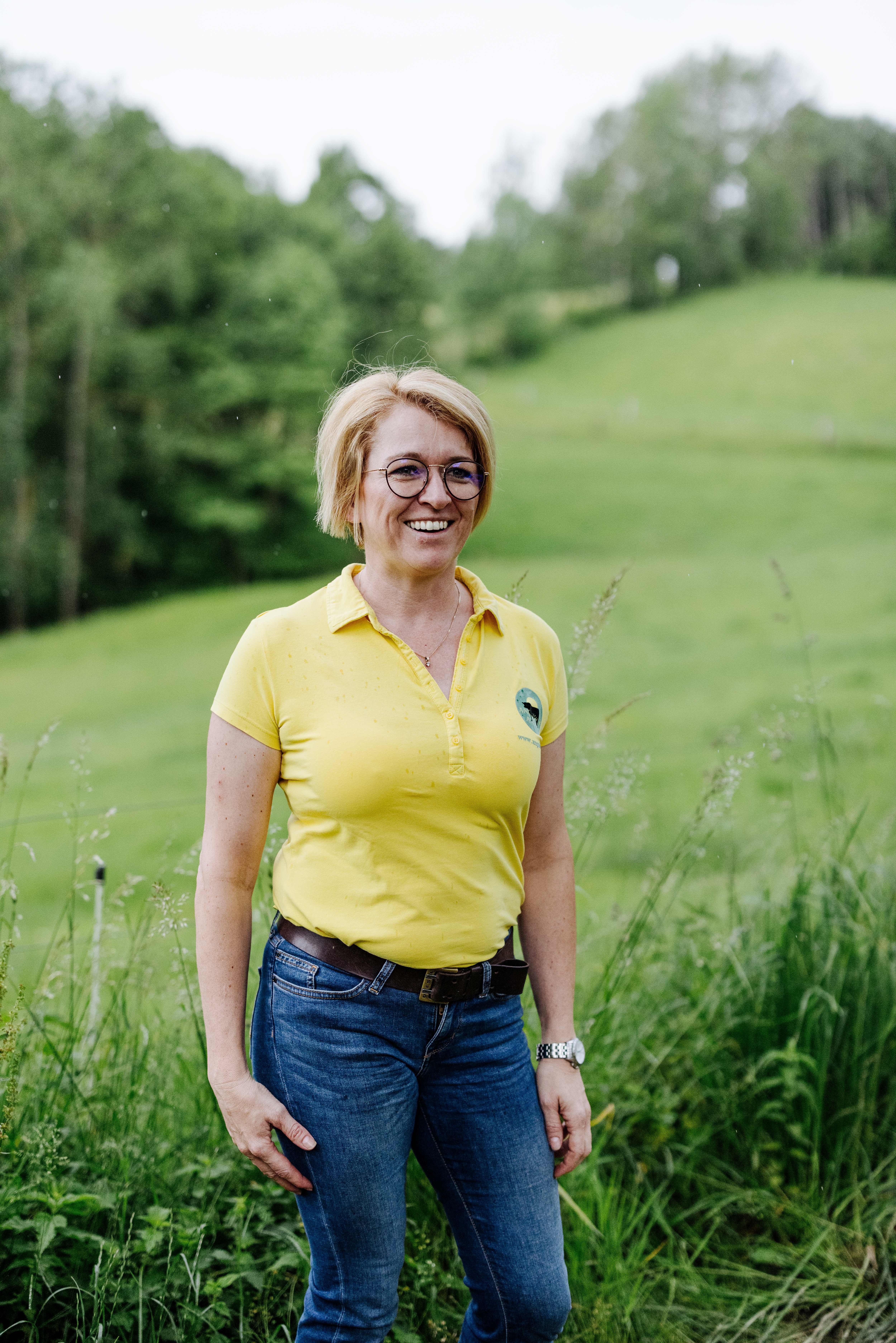 Die Besitzerin, Sandra Anderl, steht lächelnd auf einer grünen Wiese.