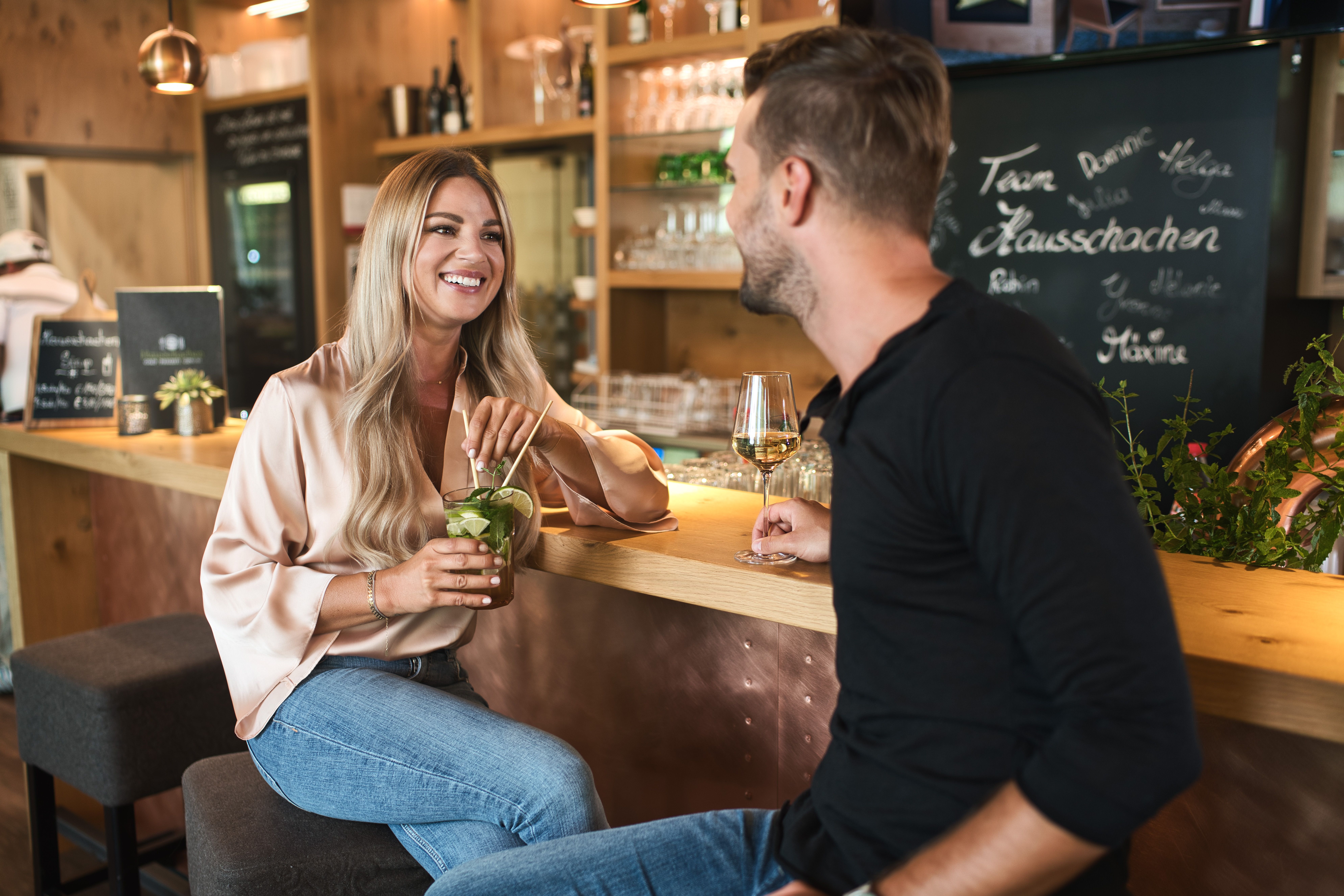 Ein Mann und eine Frau sitzen an einer Bar, die Frau hält einen Cocktail in den Händen.