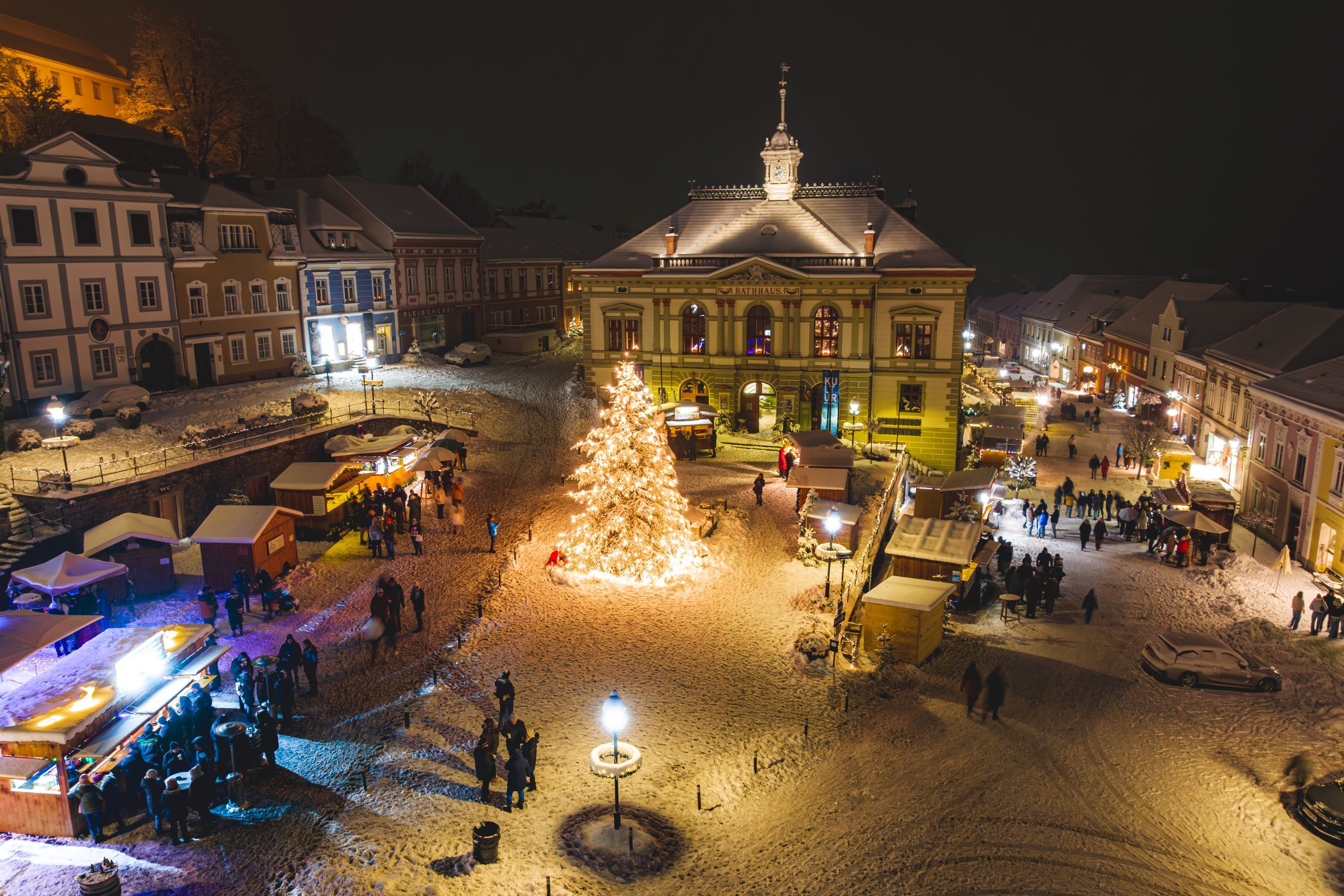 Weitraer Adventtage: Drohnenfoto abends, der Rathausplatz mit Hütten und viel Schnee ist schön beleuchtet.
