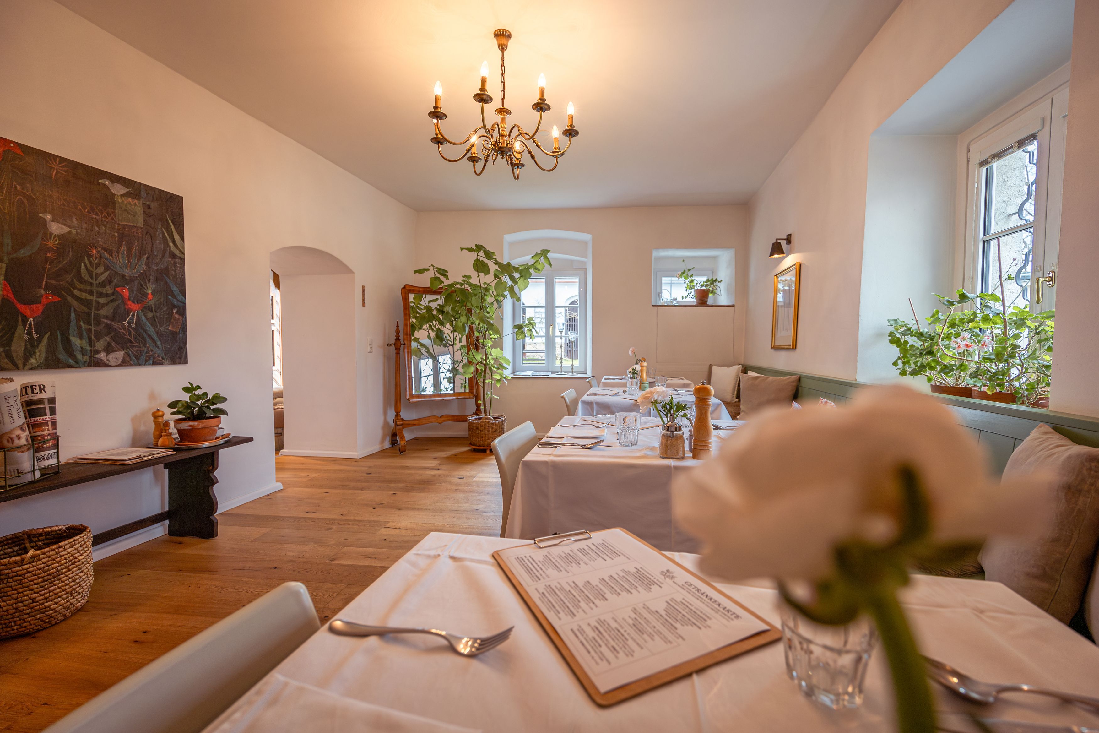 Gemütliches Restaurant mit Holzboden, weißen Tischdecken und Pflanzen.