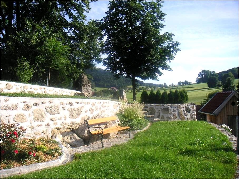 Ein Garten mit Steinmauer, Bank und Bäumen im Hintergrund.