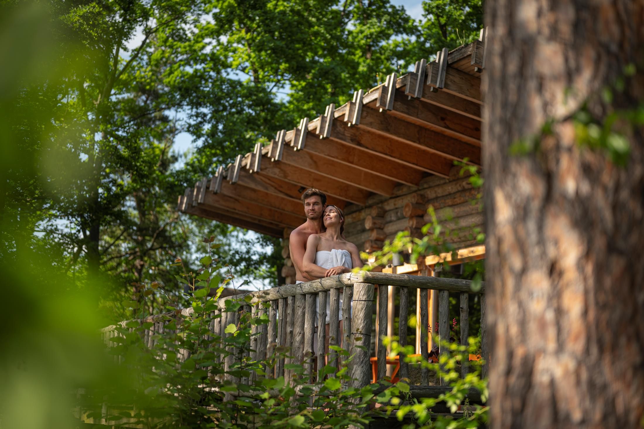 Ein Paar steht auf einem Holz-Balkon in einem Wald, umgeben von Bäumen.