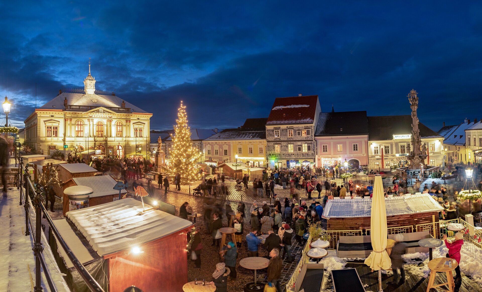 Die festlich beleuchteten Stände des Adventmarktes laden zum Verweilen ein, während der Duft von Glühwein und frisch gebackenen Leckereien in der kalten Luft schwebt. Ein großer Weihnachtsbaum erstrahlt im Zentrum und schafft eine zauberhafte Atmosphäre, die die Besucher in eine besinnliche Stimmung versetzt.