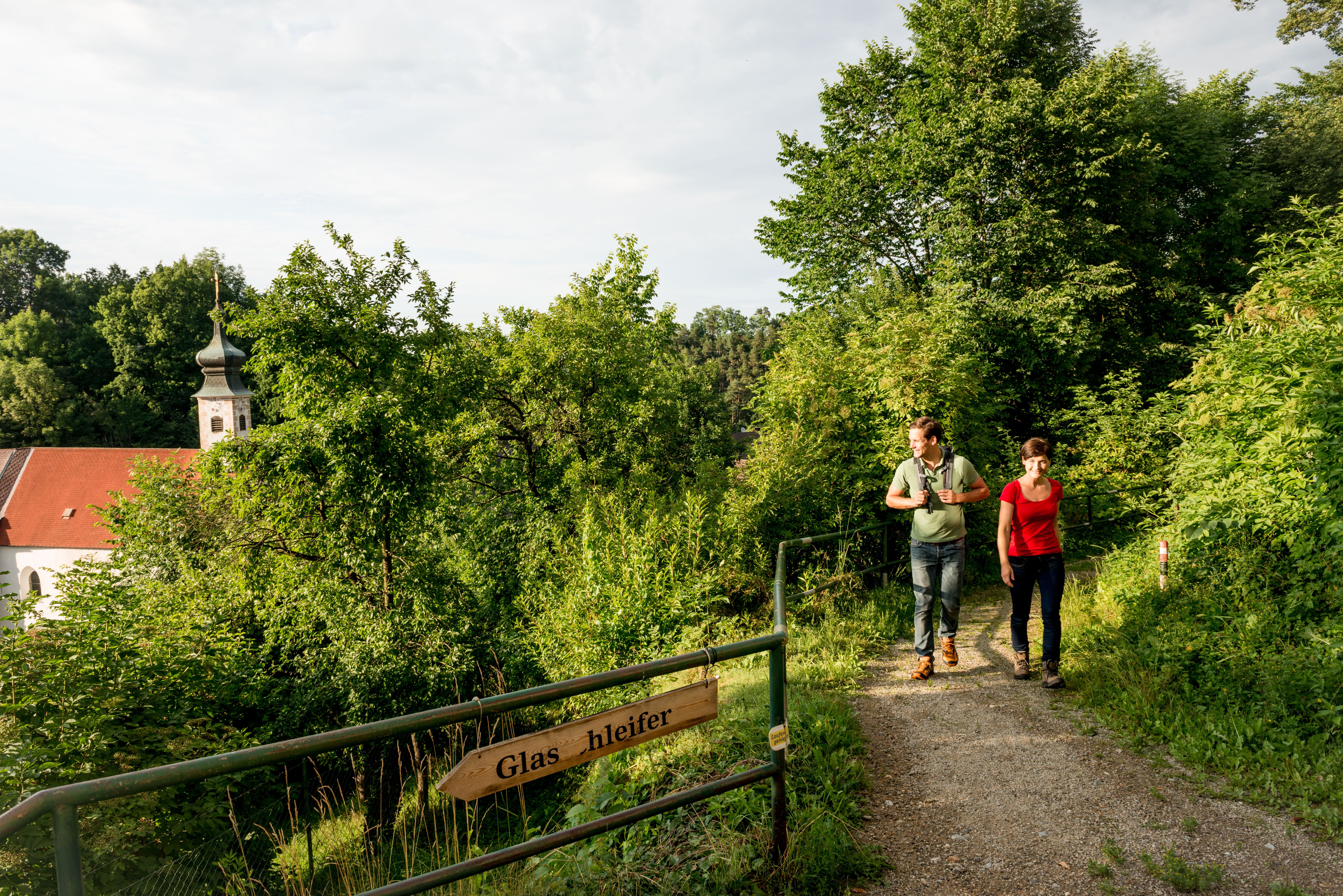 Ein Mann und eine Frau wandern durch die Natur. Im Hintergrund die Bürgerspitalkirche Weitra.