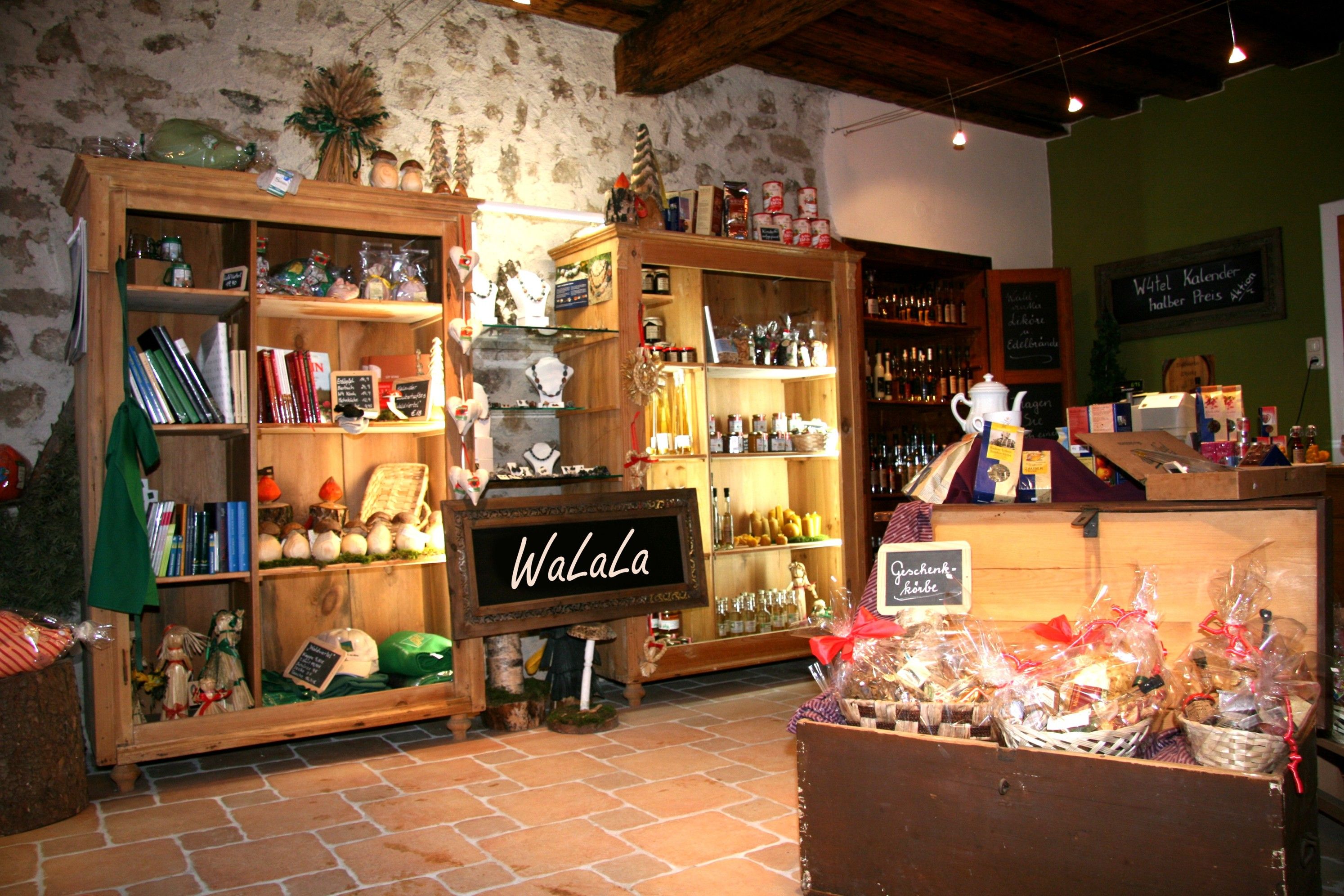 Ein gemütlicher Laden mit Holzregalen, die verschiedene Produkte und Geschenke präsentieren. Ein Schild mit der Aufschrift 'WaLaLa' ist sichtbar.