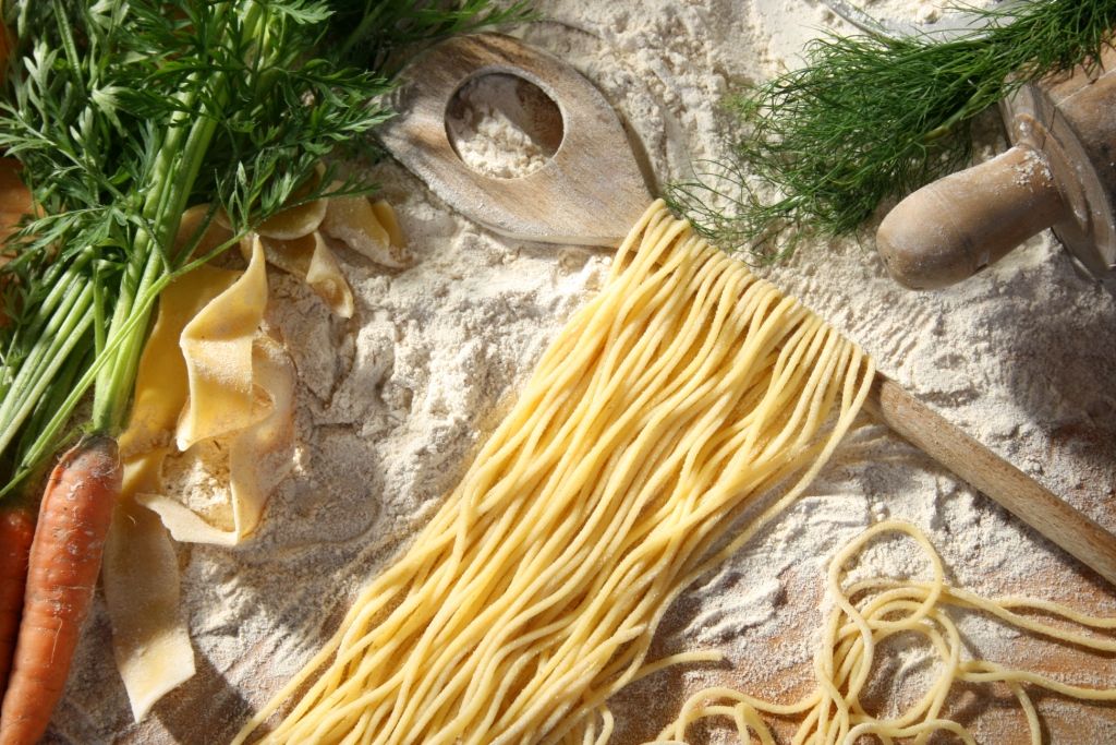Detailbild: frische Teigwaren auf Mehl, links eine Karotte